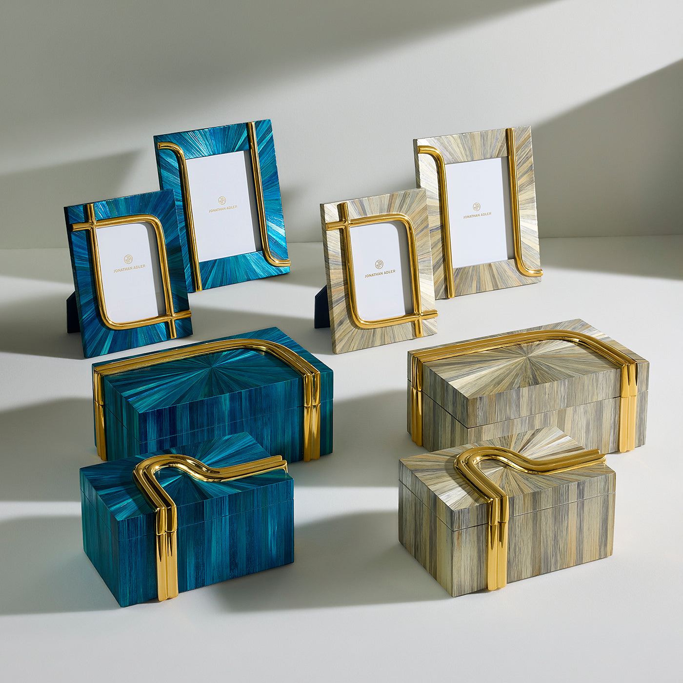 A set of decorative picture frames and matching boxes with an inlaid wood and gold finish, displayed on a light gray surface with dramatic shadows.