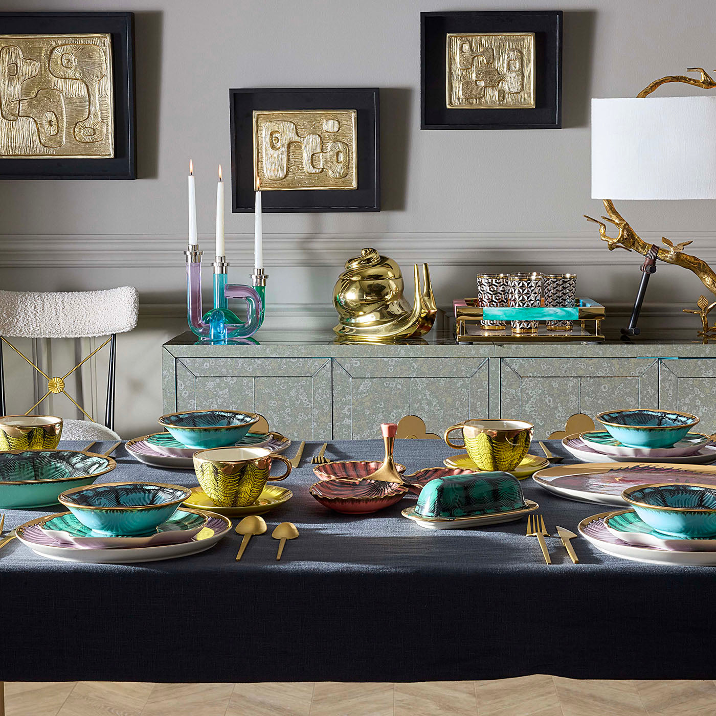 Dining table set with gold and blue tableware, candles, and decorative items in a stylish room.