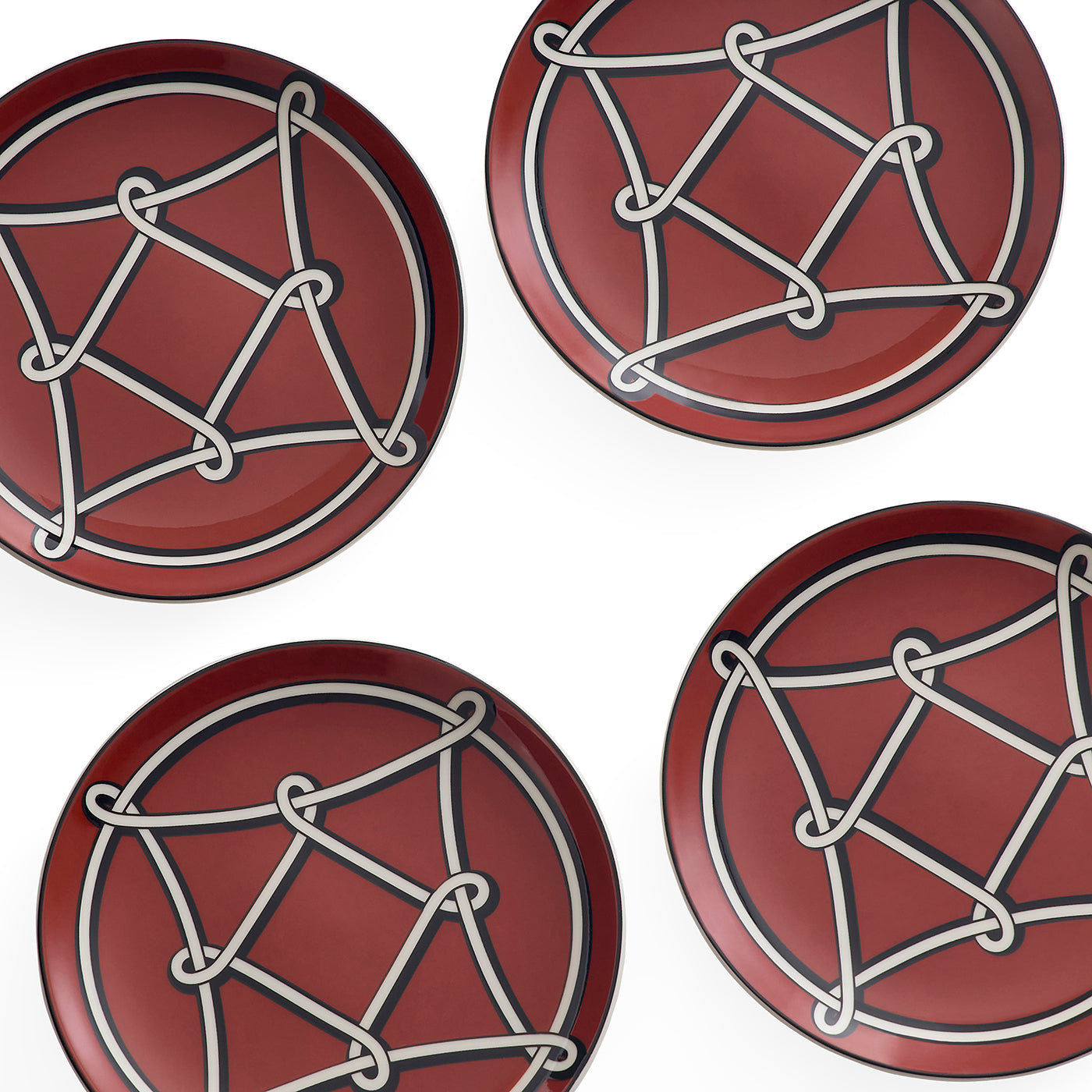 Four round red plates arranged in a grid on a white background, each decorated with a white geometric knot-like pattern and a thin dark blue border.