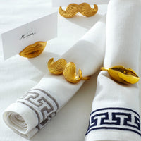 Gold mustache and lip-shaped napkin rings on white napkins with decorative patterns.