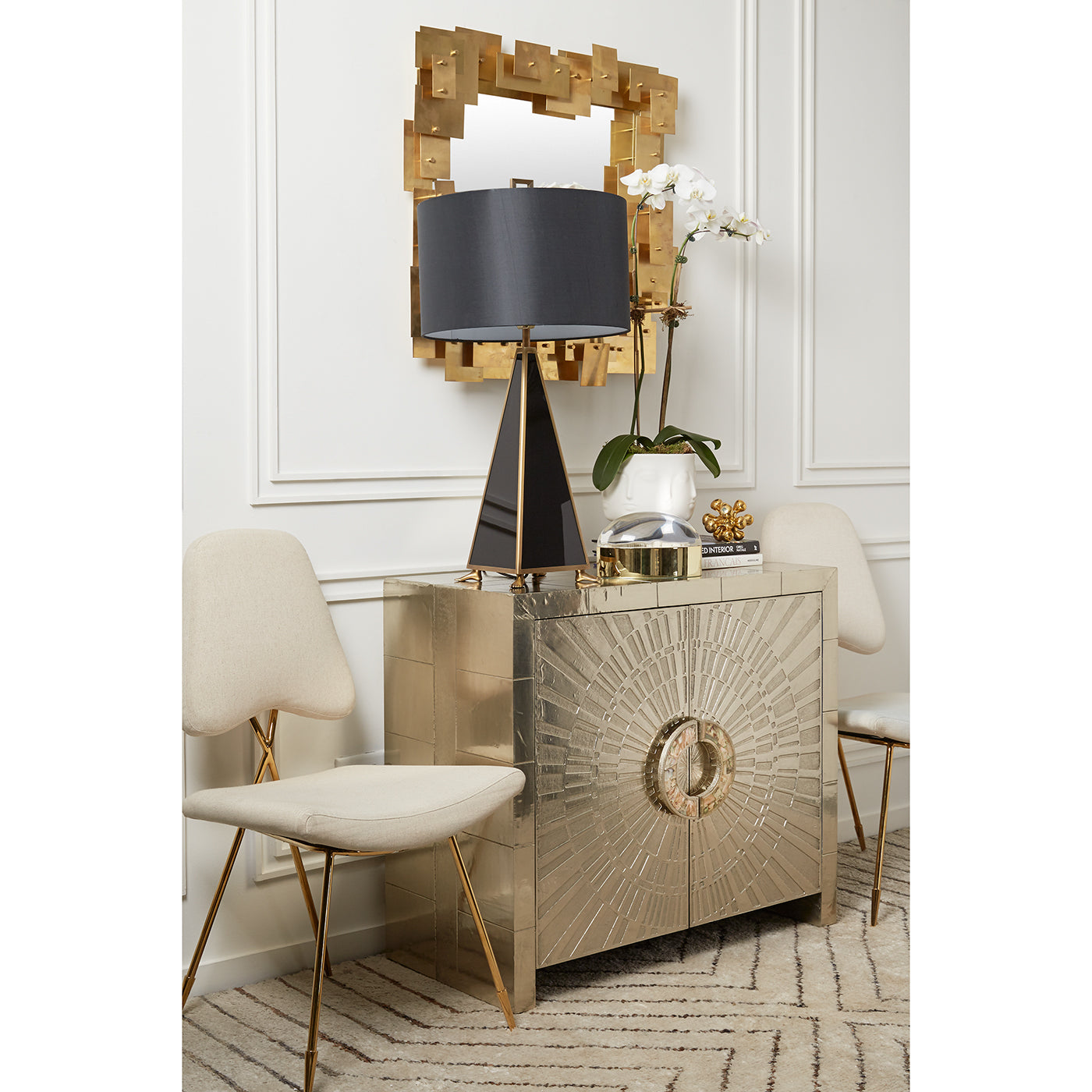 Decorative console table with gold accents, black lamp, and white chairs in a room.
