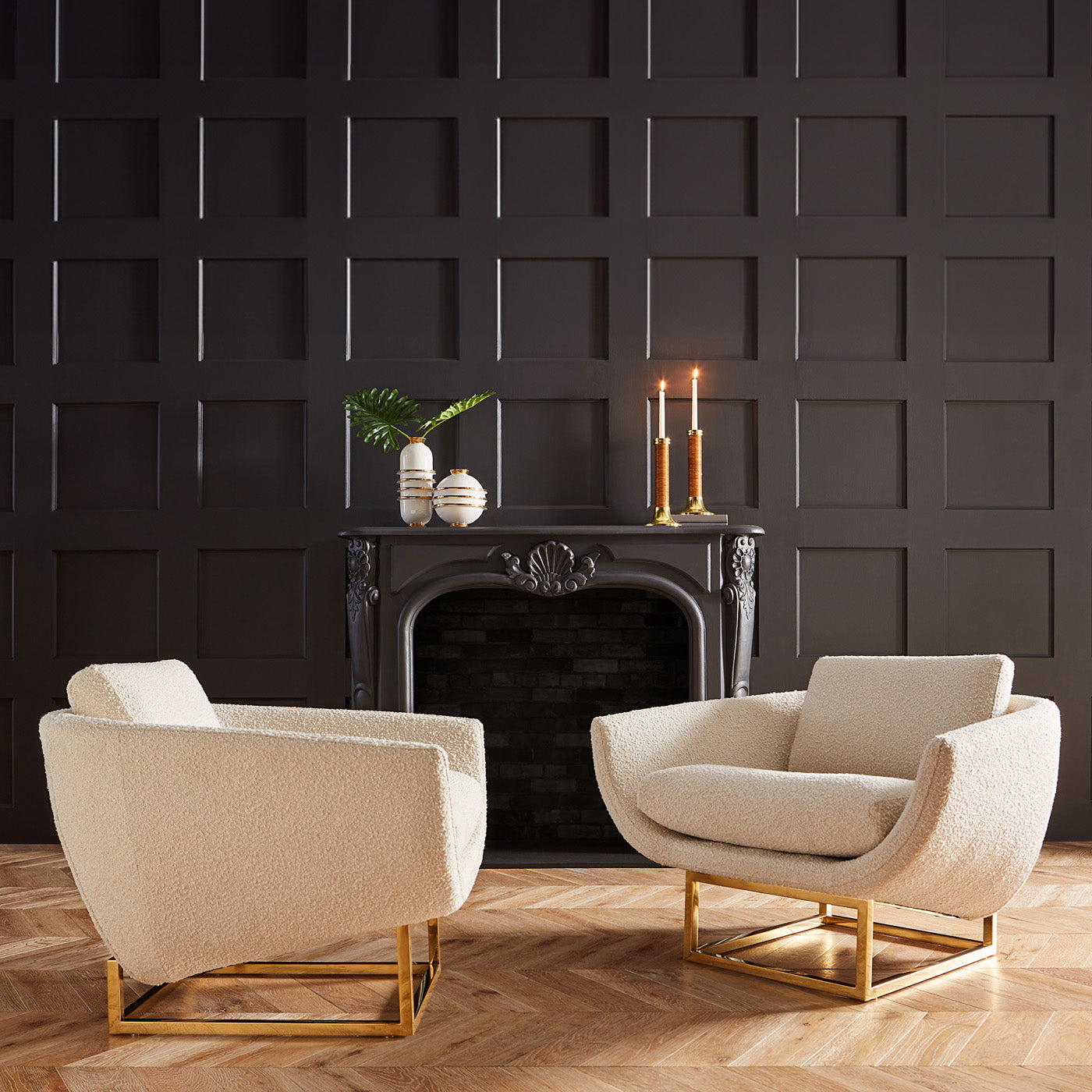 Two beige armchairs in a room with a dark paneled wall and fireplace.