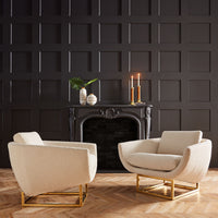 Two beige armchairs in a room with a dark paneled wall and fireplace.