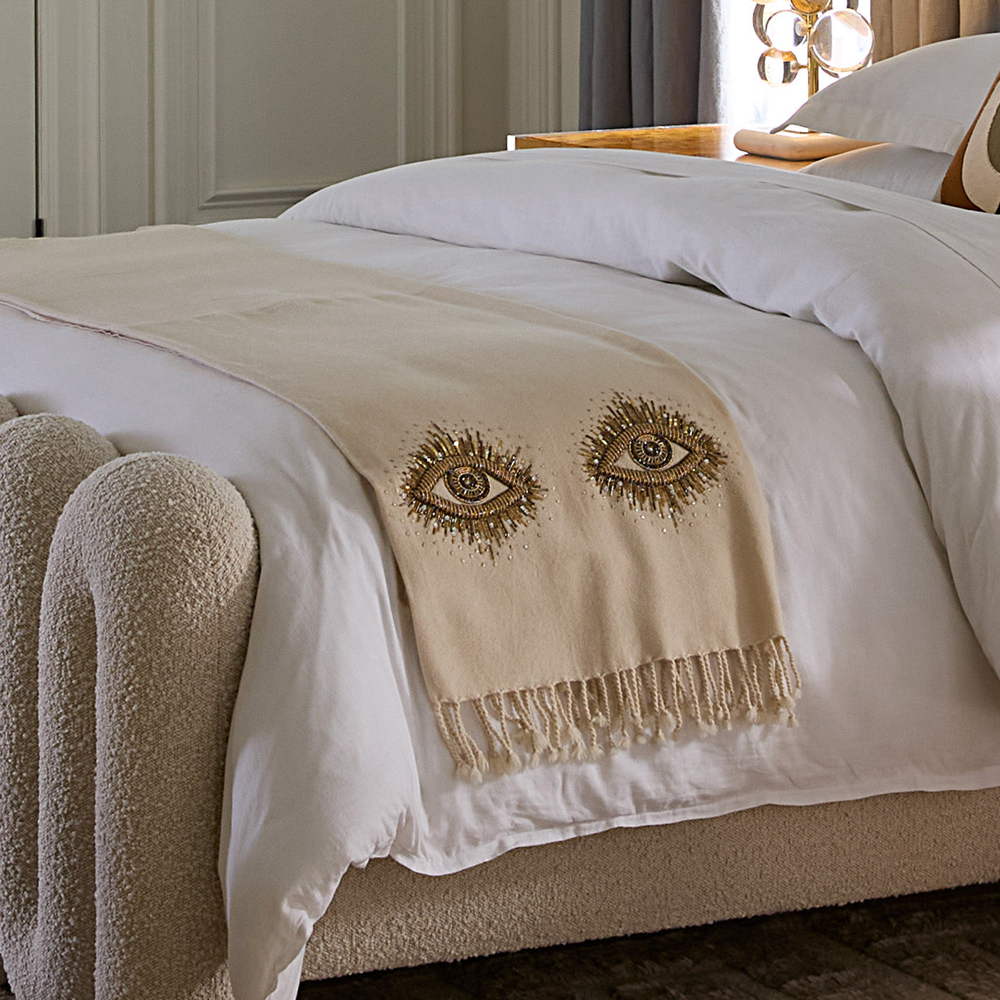Beige blanket with embroidered eyes on a bed in a bedroom setting