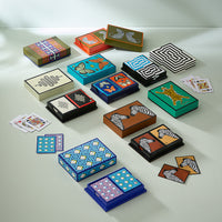 An assortment of colorful playing cards and matching decorative boxes arranged on a light gray surface. The sets feature various patterns including zebra prints, stripes, geometric designs, butterflies, and abstract shapes in blue, green, orange, black, white, and brown.