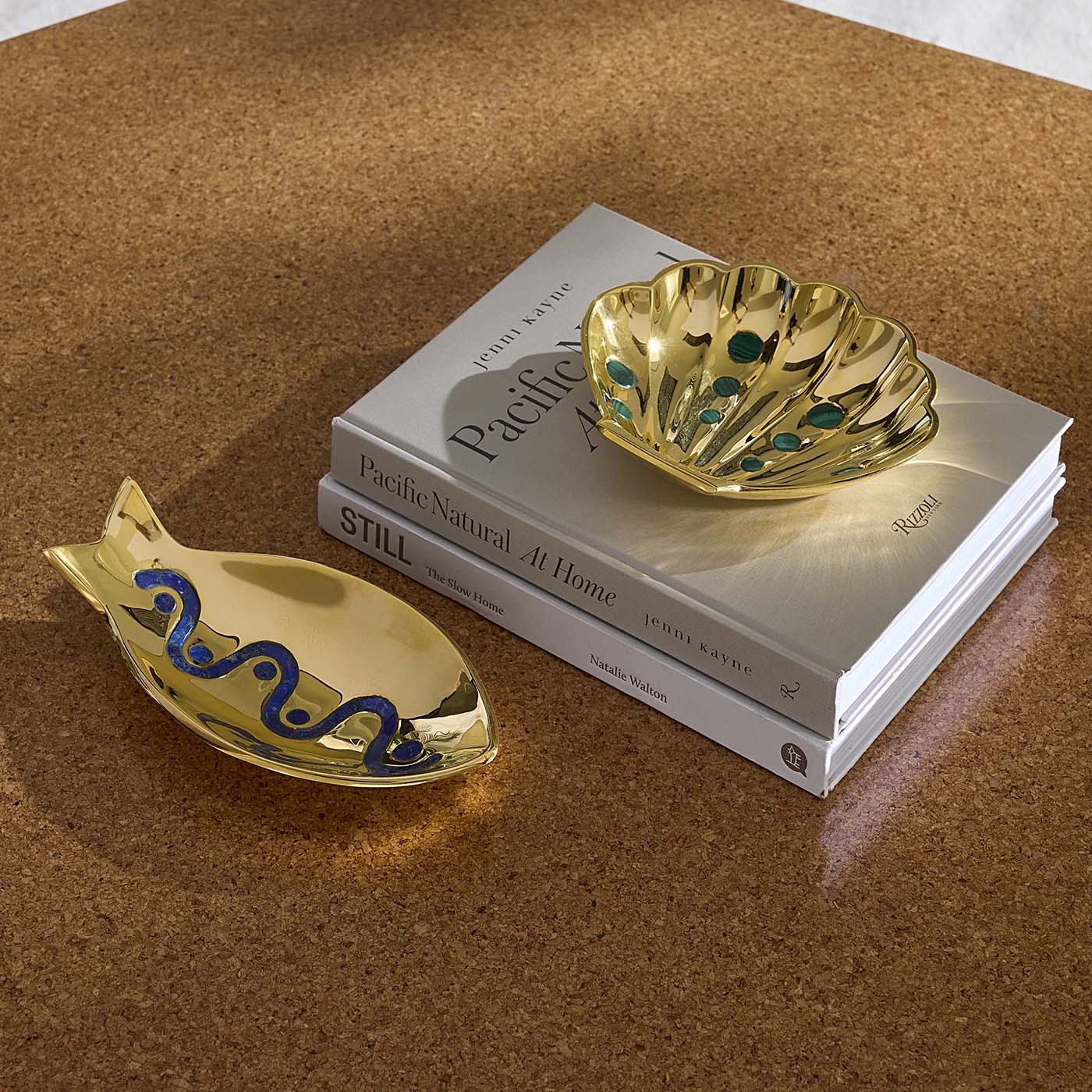Gold fish and shell-shaped trinket dishes on a stack of books with a brown surface.