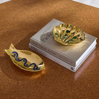 Gold fish and shell-shaped trinket dishes on a stack of books with a brown surface.
