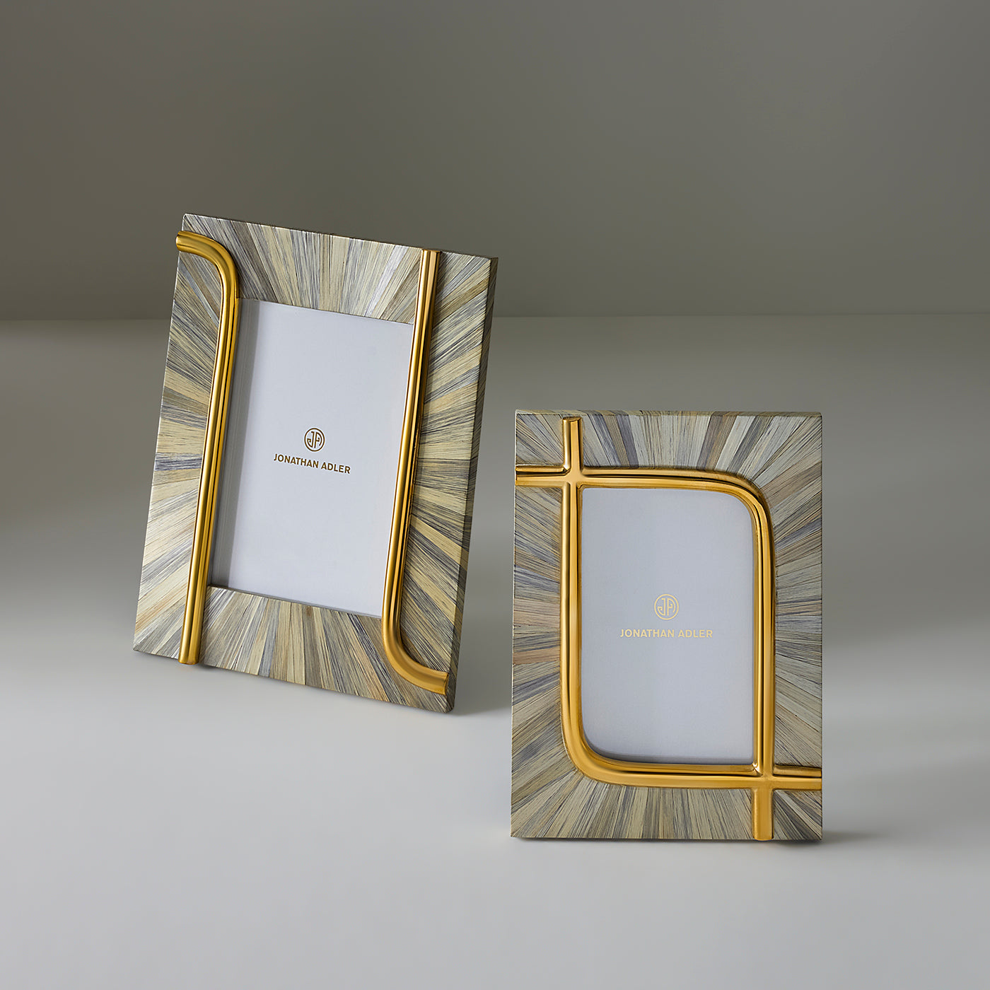 Two Jonathan Adler picture frames with a metallic gold and gray sunburst pattern, displayed on a neutral gray background.