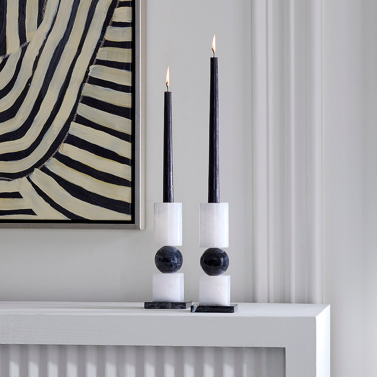set of two geometric black and white candle stick holders styled with lit black candlesticks (not included) on a mantel next to abstract art 