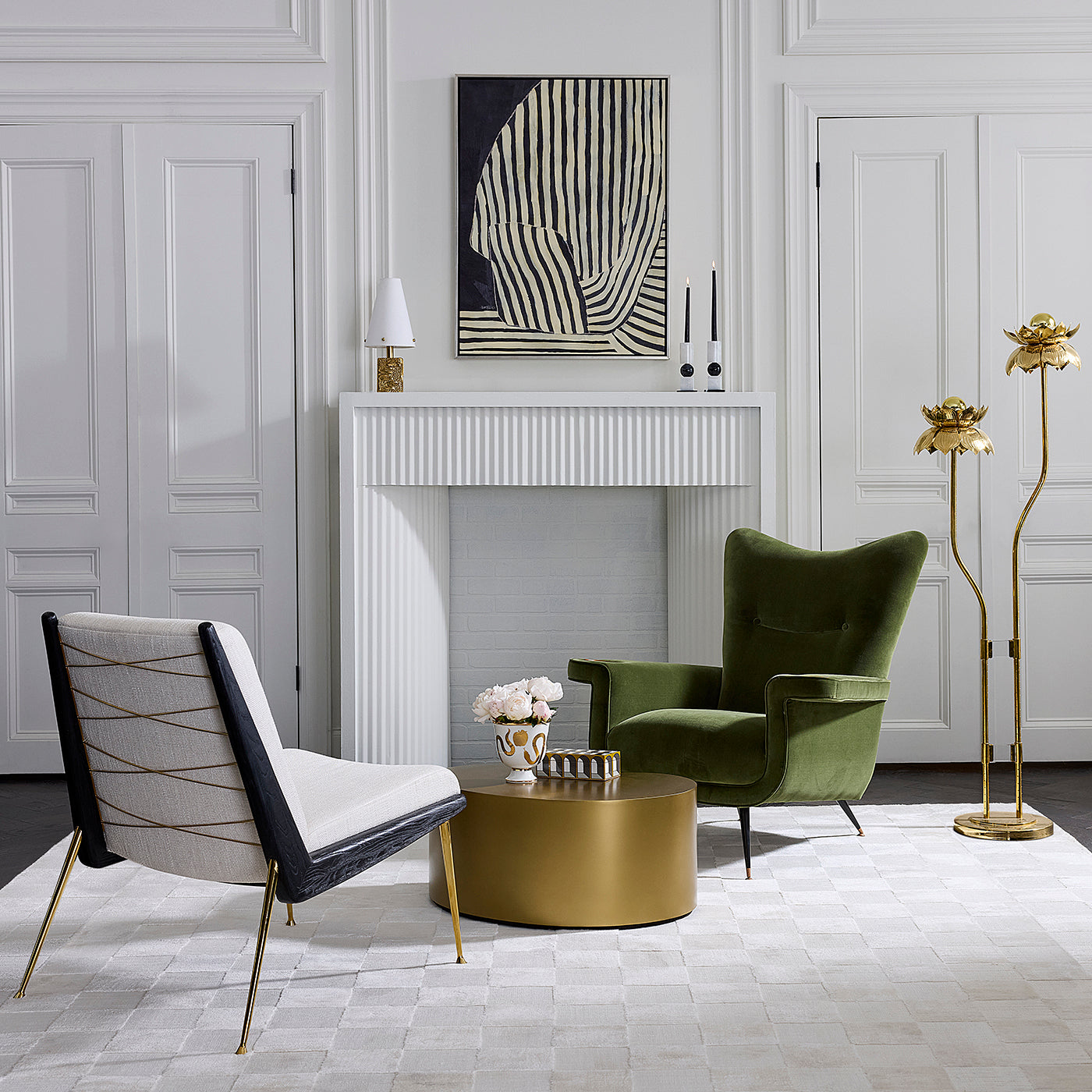 A styled interior scene with two lounge chairs, a round gold coffee table, a white fireplace, and decorative wall art in a bright, elegant room.