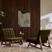 A styled interior scene with two mid-century modern armchairs in dark olive green velvet, set in front of a dark wood slatted wall with a framed abstract art print. A small side table with a drink sits between them, and a lamp is visible on the right.