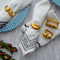 White napkins with gold napkin rings on a gray surface with decorative elements.
