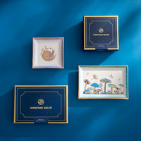 Decorative trays with artistic designs on a blue background, featuring the brand 'Jonathan Adler'.