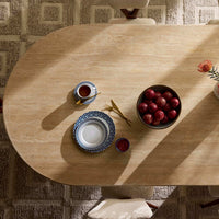 Wooden table with a cup, saucer, bowl of apples, and other items on a textured floor.