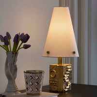 Decorative lamp with textured base on a table next to a vase with purple tulips and a patterned glass.