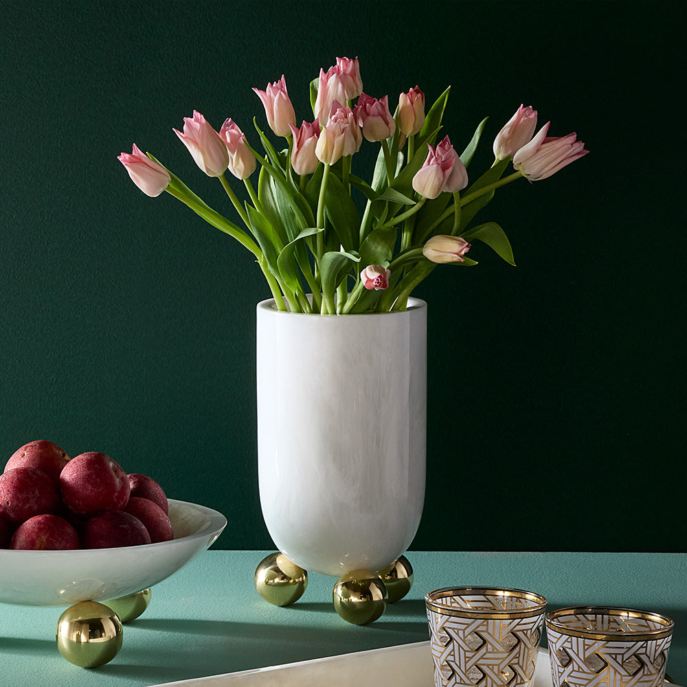 White vase with pink tulips on a green surface with decorative items.