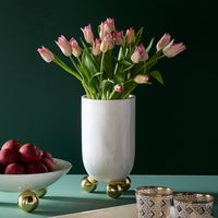 White vase with pink tulips on a green surface with decorative items.
