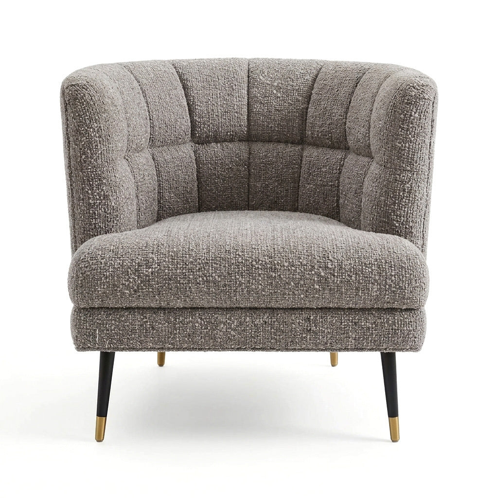 A modern barrel-style accent chair upholstered in a textured gray bouclé fabric, featuring channel-tufted detailing on the backrest and seat, black tapered legs, and gold-tone metal foot caps, shown against a plain white background.