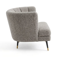 A modern curved armchair upholstered in a textured gray bouclé fabric, featuring tapered black legs with gold metal tips, shown against a plain white background.