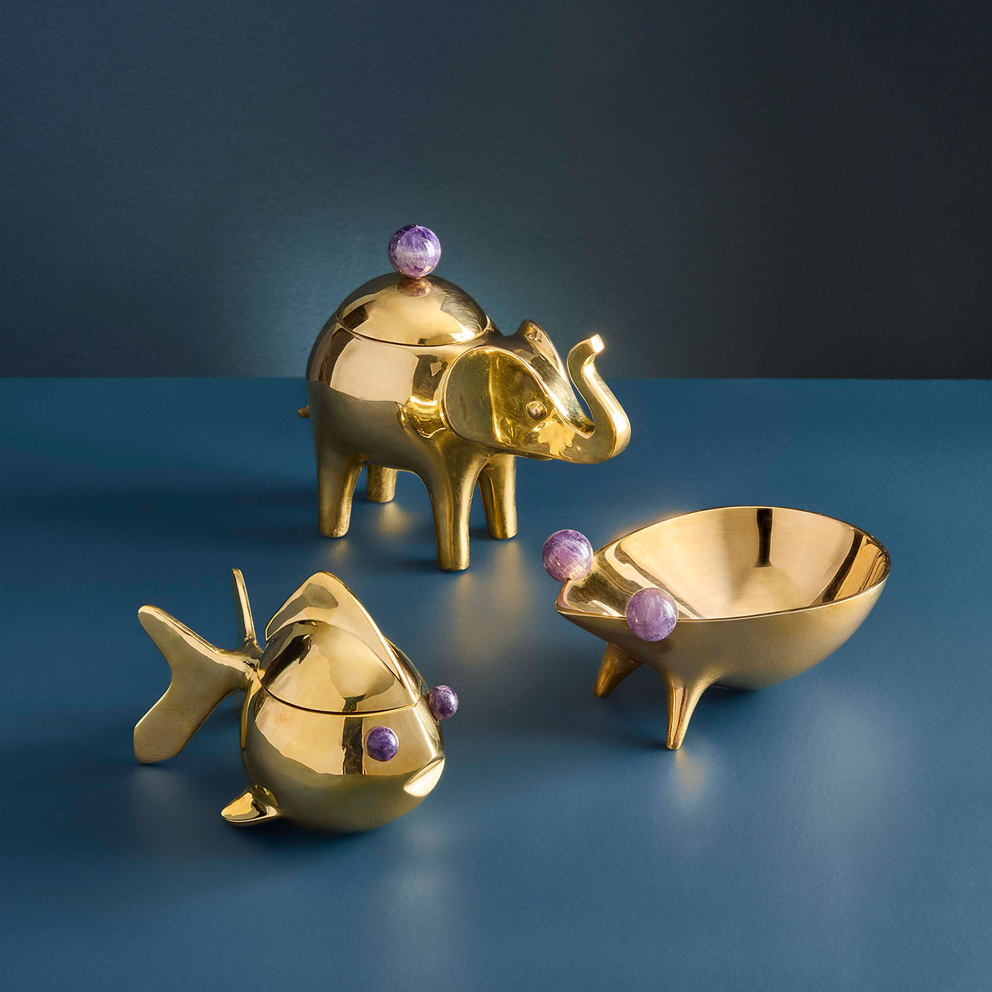 Gold elephant, fish, and bowl with purple gemstones on a blue background