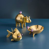 Gold elephant, fish, and bowl with purple gemstones on a blue background