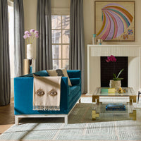 Modern living room with a blue sofa, glass coffee table, and colorful abstract painting.