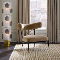 Beige chair with black metal legs in a room with a tall floor lamp and large window.