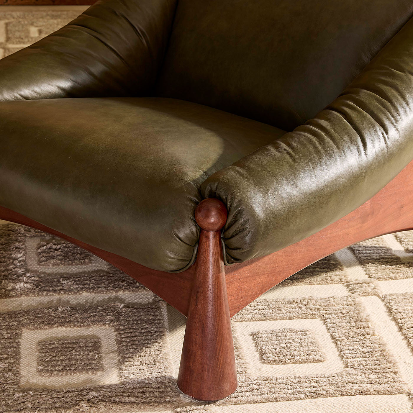 Close-up of a green leather chair with wooden leg on a patterned carpet