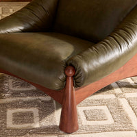 Close-up of a green leather chair with wooden leg on a patterned carpet