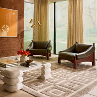 Modern living room with green leather chairs, a patterned rug, and decorative elements.