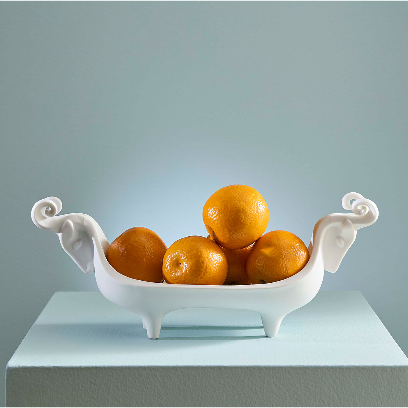 White decorative bowl with oranges on a light blue surface and background