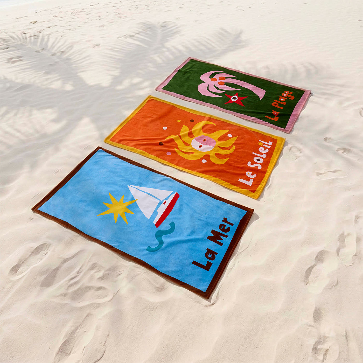 Three colorful beach towels with ocean-themed designs on a sandy background