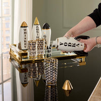 Person holding a bottle labeled 'Vodka' on a decorative tray with patterned glasses.