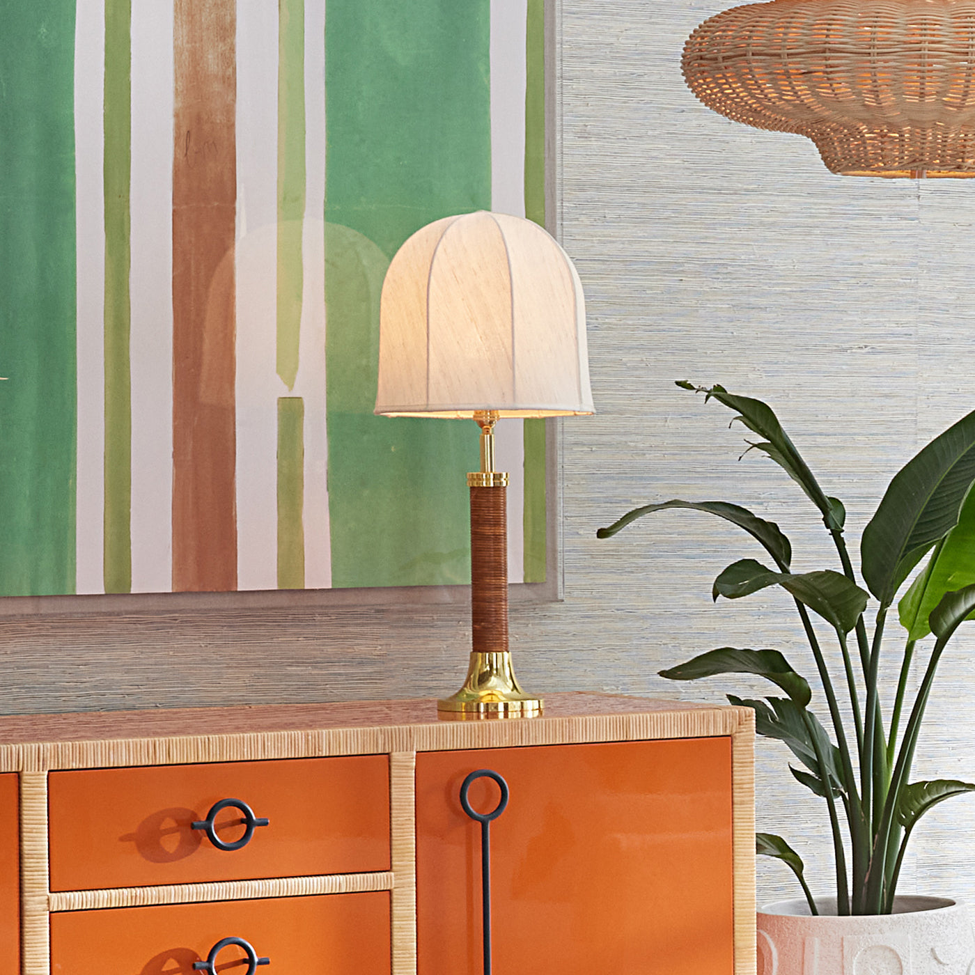 Table lamp on an orange cabinet with a striped wall and plant in the background