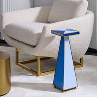 A modern geometric side table with a blue and white triangular design and gold brass trim, styled next to a cream bouclé armchair with a gold base.