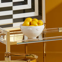 Bowl of lemons on a glass table with gold legs against a striped wall.