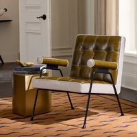 A modern accent chair with olive green tufted leather and cream fabric upholstery, supported by black metal legs, styled in a room next to a gold side table.