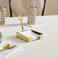 Dining table setting with gold cutlery, geometric-patterned glasses, and a napkin holder.