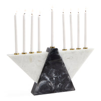 A modern Hanukkah menorah made of white and black marble with gold-tone metal candle holders, holding nine white taper candles that are lit, set against a solid white background.