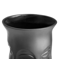 A close-up of a matte black ceramic tiki mug with a textured, stylized face design, shown against a plain white background.