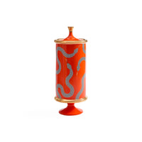 A tall cylindrical ceramic lidded jar or candle holder in bright orange-red, decorated with wavy dotted silver-gray patterns and accented with gold-toned trim at the top, bottom, and base.