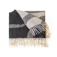 A folded woven throw blanket with cream fringe, featuring a geometric pattern in black, gray, and cream on a white background.