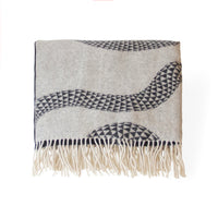 A rectangular woven throw blanket with cream-colored fringe, featuring a light beige base with dark gray geometric wavy patterns and fringed edges, displayed flat against a white background.