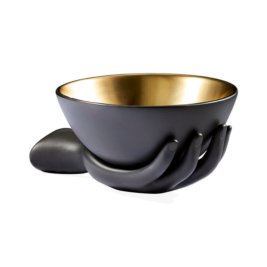 A matte black ceramic bowl with a metallic gold interior, supported by sculpted hands in a cup holder design, shown on a white background.