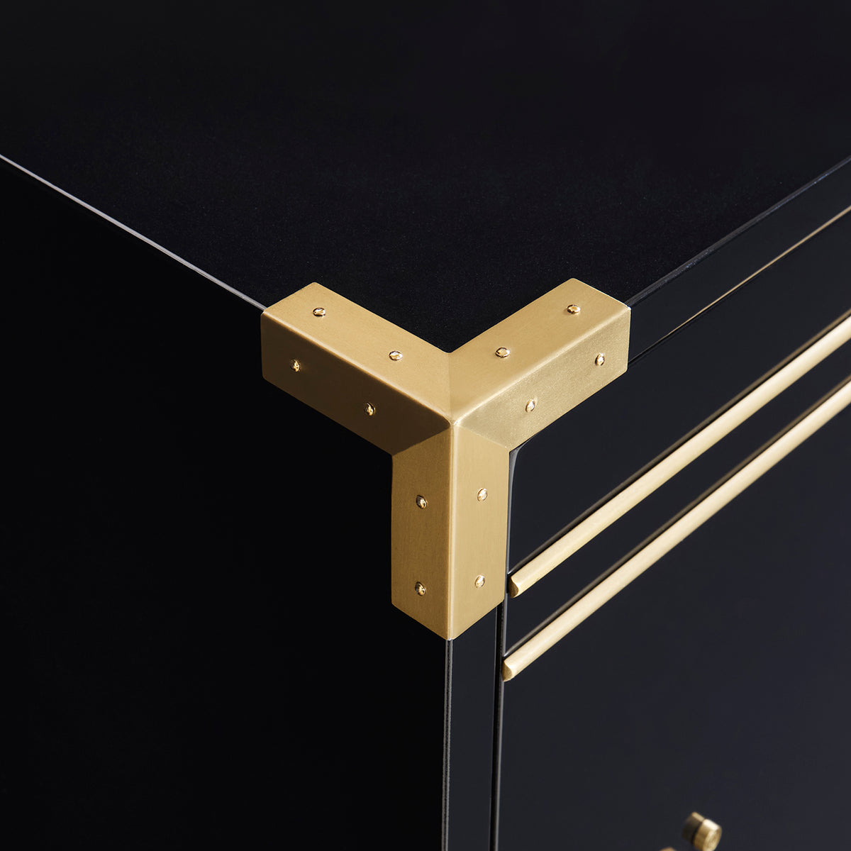 Close-up of a black cabinet corner with a brushed gold metal L-shaped corner protector and matching gold drawer pulls.