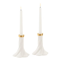 Two white taper candles in sculptural flared holders with gold bands, shown on a plain white background.