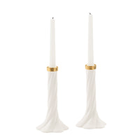 A pair of white taper candle holders with a twisted flared base and a thin gold band near the top, each holding a white taper candle, shown on a plain white background.