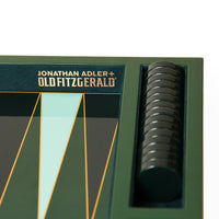 Close-up of a Jonathan Adler + Old Fitzgerald board game box corner, showing dark green packaging with gold lettering and a stack of round black pieces in a side slot.