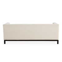 A modern upholstered sofa shown from the back, featuring a cream-colored textured fabric backrest and a low black metal frame, set against a plain white background.
