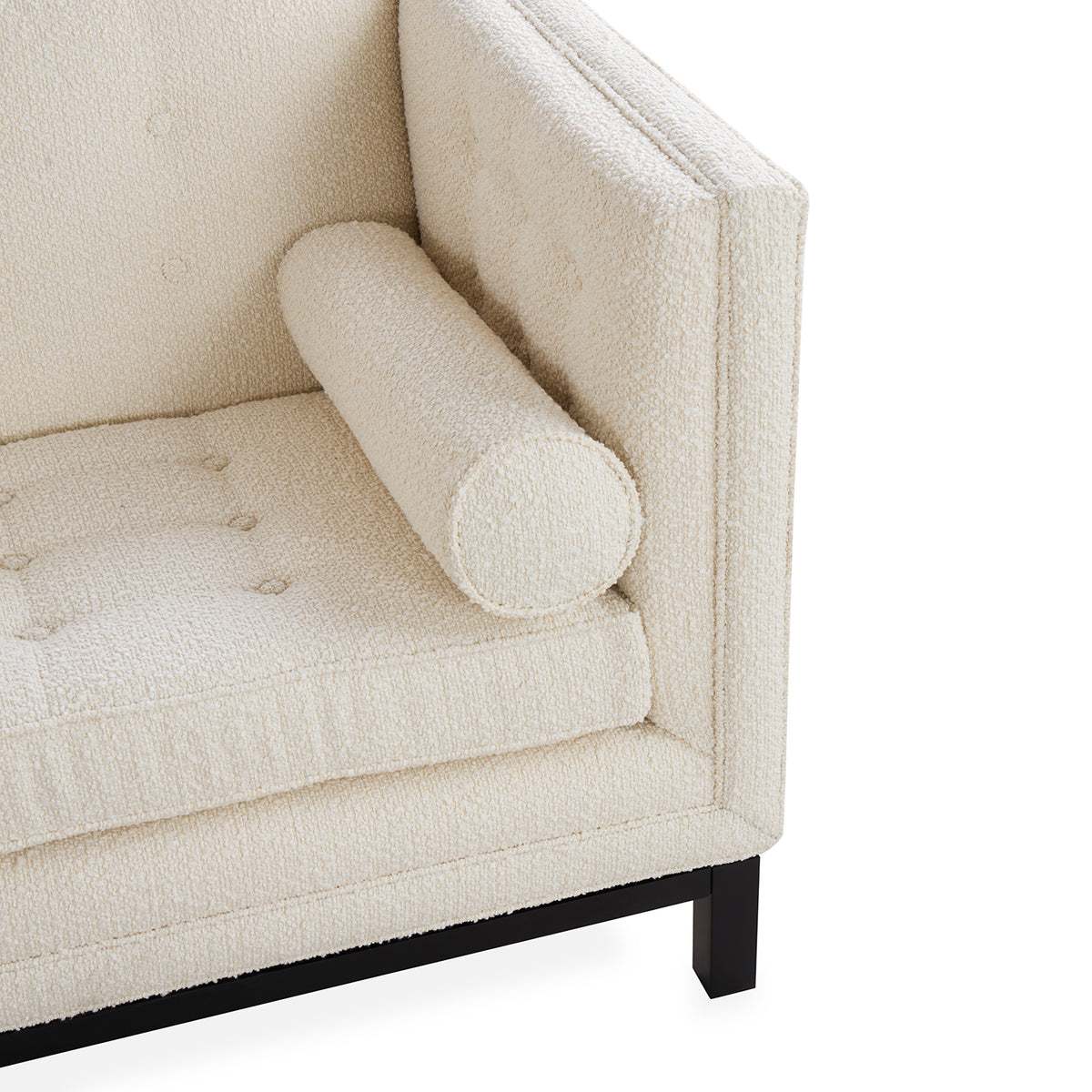 Close-up of a cream bouclé armchair corner with a cylindrical bolster armrest, tufted seat cushion, and black wooden legs on a white background.